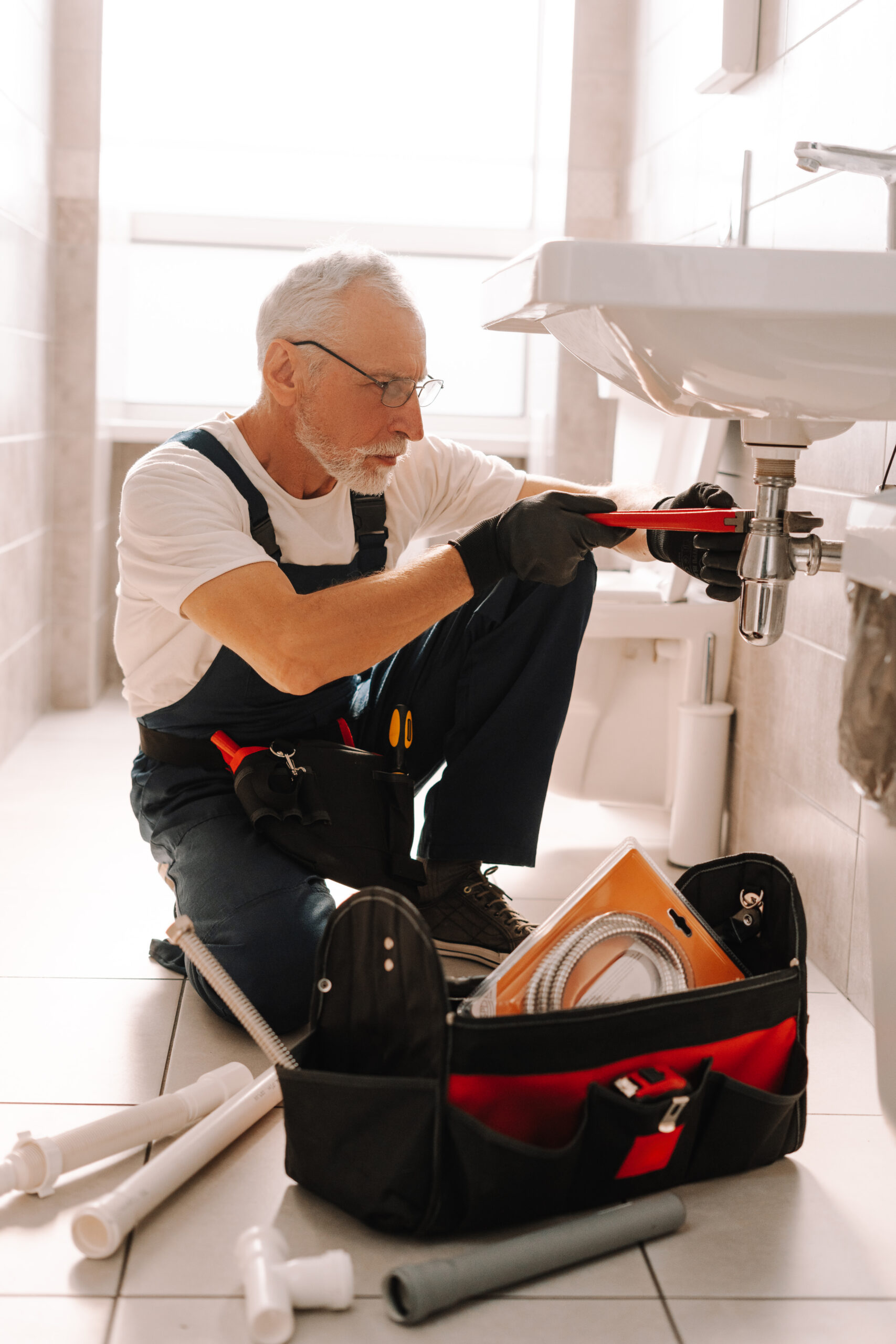 senior plumber installing sink using adjustable wrench bathroom scaled